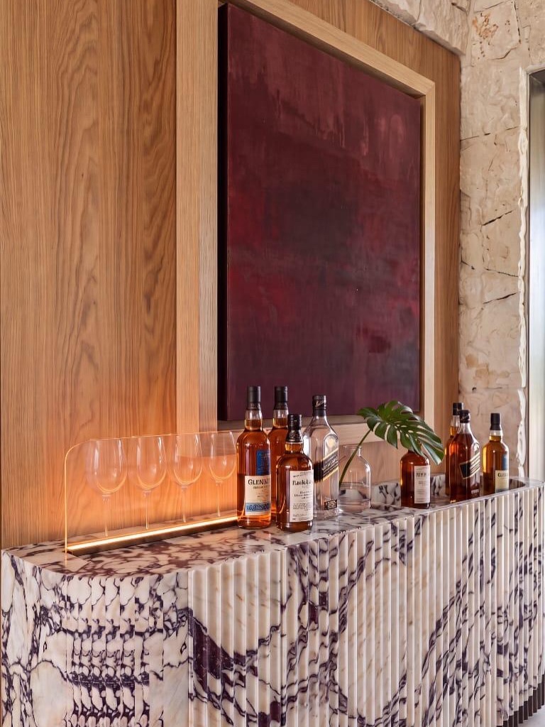 Marble sideboard bar with lit bottles and glasses in front of a wooden panel, rendered with Vizai